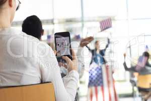 Businessman taking photo of businesswoman doing speech in conference room