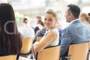 Young Caucasian businesswoman sat in conference room, smiling to camera
