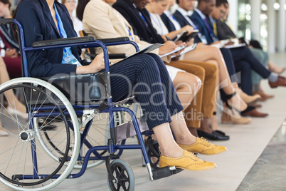 Business people sitting on chairs while listening to speech in conference room