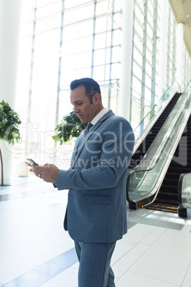 Mature businessman looking at mobile phone while standing in modern office