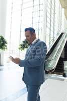 Mature businessman looking at mobile phone while standing in modern office