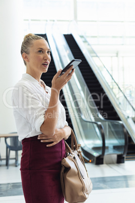 Young Caucasian businesswoman speaking on mobile phone while standing in modern office