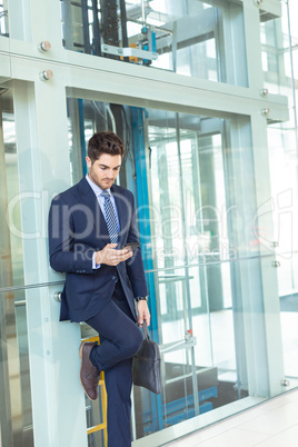 Young Caucasian businessman looking at mobile phone while standing in modern office