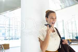 Female executive speaking on mobile phone while standing in modern office