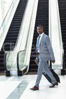 Young African-american executive walking with suitcase in hall