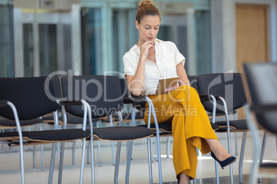 Young Caucasian female executive looking at digital tablet while sitting on chair in empty conferenc