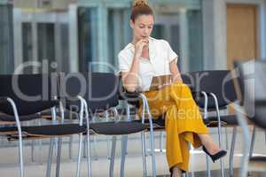 Young Caucasian female executive looking at digital tablet while sitting on chair in empty conferenc