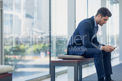 Caucasian businessman looking at mobile phone while sitting on bench in modern office.