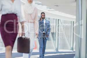 African american businessman walking in corridor while talking in mobile phone in modern office