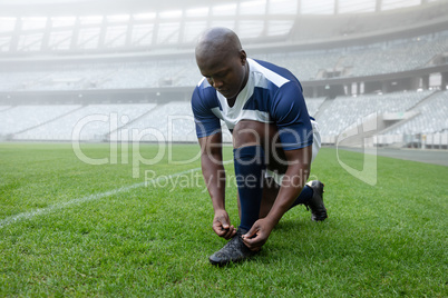 African american male rugby player tying shoelaces in the stadium