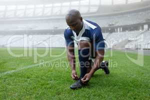 African american male rugby player tying shoelaces in the stadium