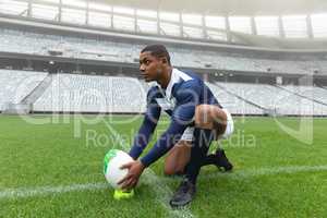 African American male rugby player placing rugby ball on a stand in stadium