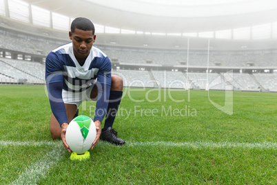 African American male rugby player placing rugby ball on the stand in stadium