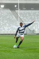 African American male rugby player kicking rugby ball in stadium