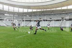 African American male rugby player kicking rugby ball in stadium.