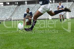 African American male rugby player kicking rugby ball in stadium