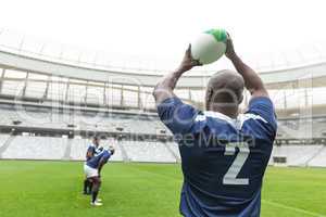 African American male rugby player throwing rugby ball in stadium