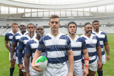 Group of diverse male rugby players standing together with rugby ball in stadium