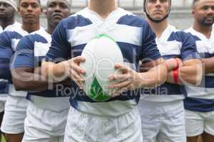Group of diverse male rugby players standing together with rugby ball in stadium