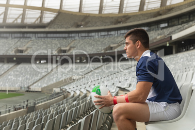 Caucasian male rugby player sitting with rugby ball in stadium