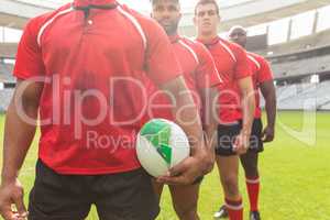 Male rugby players standing together with rugby ball in stadium