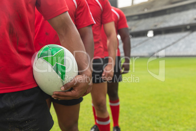 Male rugby players standing together with rugby ball in stadium