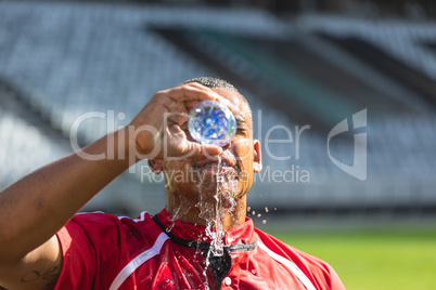 Rugby player pouring water from water bottle on his face in stadium