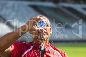 Rugby player pouring water from water bottle on his face in stadium