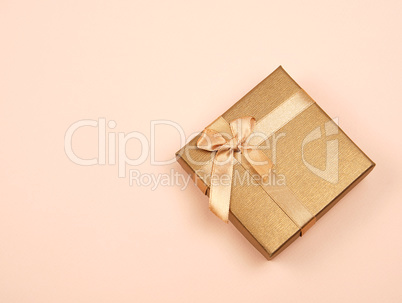 closed golden gift box with a bow on a beige background