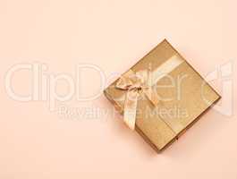 closed golden gift box with a bow on a beige background