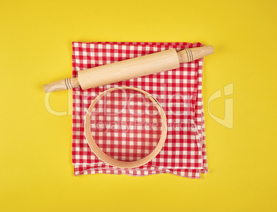 new wooden rolling pin on a red textile napkin and a round sieve