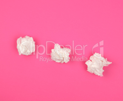 three crumpled white paper napkins on a pink background