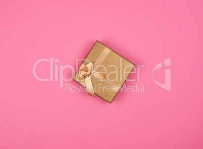 closed golden gift box with a bow on a pink background
