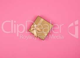 closed golden gift box with a bow on a pink background