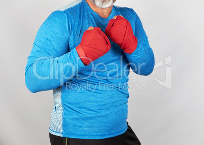 adult athlete in blue clothes, hands wrapped in a red elastic ba