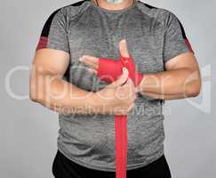 athlete stand in gray clothes and wrap his hands in red textile