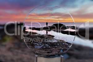 Lone man through a crystal ball on the rocks at sunset at Treasu