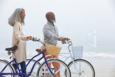 Couple smiling while holding bicycles at the beach