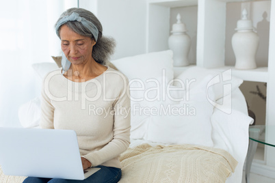 Woman sitting on a couch in a white room while using a white laptop