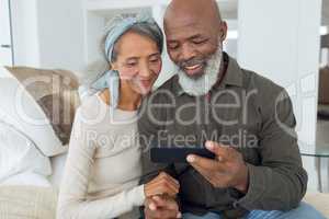 Couple sitting on a couch inside a room while looking at smartphone