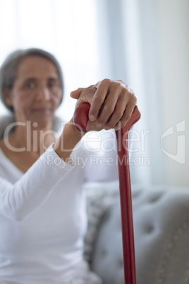 Woman sitting on couch while holding a brown walking stick