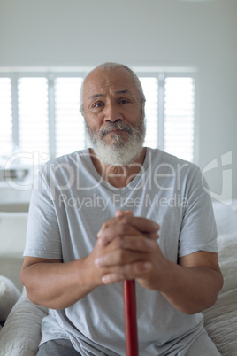 Man sitting on the bed while holding a wooden walking stick