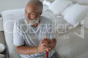 Man sitting on the bed while holding a wooden walking stick