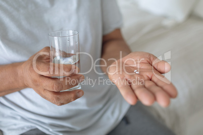 Man sitting on the bed while holding pills and a glass of water