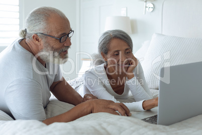 Couple sitting on bed inside a room and watching laptop