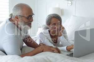 Couple sitting on bed inside a room and watching laptop