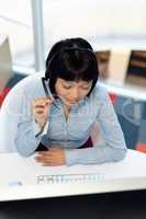 Asian Female customer service executive talking on headset at desk