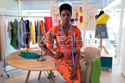 Female fashion designer sitting with hand on hip in design studio