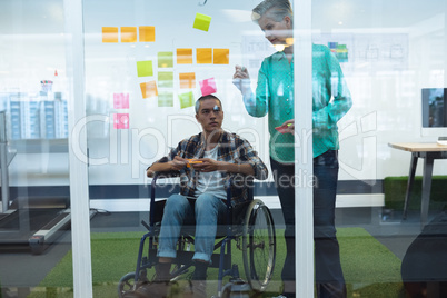 Male and female executives discussing over sticky notes in office