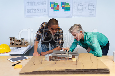 Male and female architects discussing over model structure of house at desk